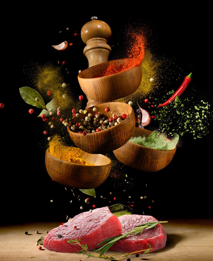 Raw beef steaks on wooden table with various spices and herbs flying with splash over black background